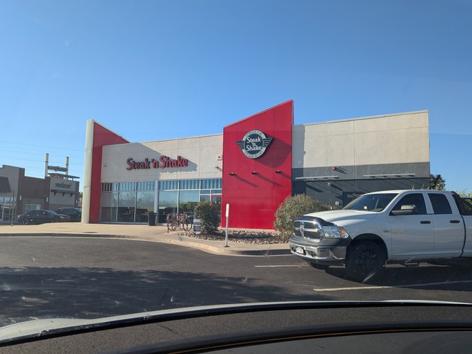 The exterior of a 'Steak 'n Shake' restaurant building with red and white architecture, with a white pickup truck parked in the foreground.