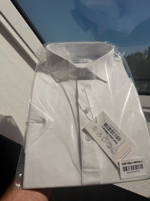 A packaged white men's dress shirt with a tag reading 'S&P-Men-White-L' is held up against a window.