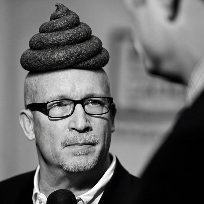 A black-and-white portrait of a bald man with glasses and a goatee, humorously edited to have a coiled pile of feces stacked on top of his head.