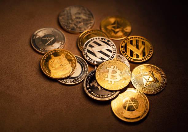 A collection of physical cryptocurrency coins, including Bitcoin, Litecoin, and Dogecoin, scattered on a dark surface.