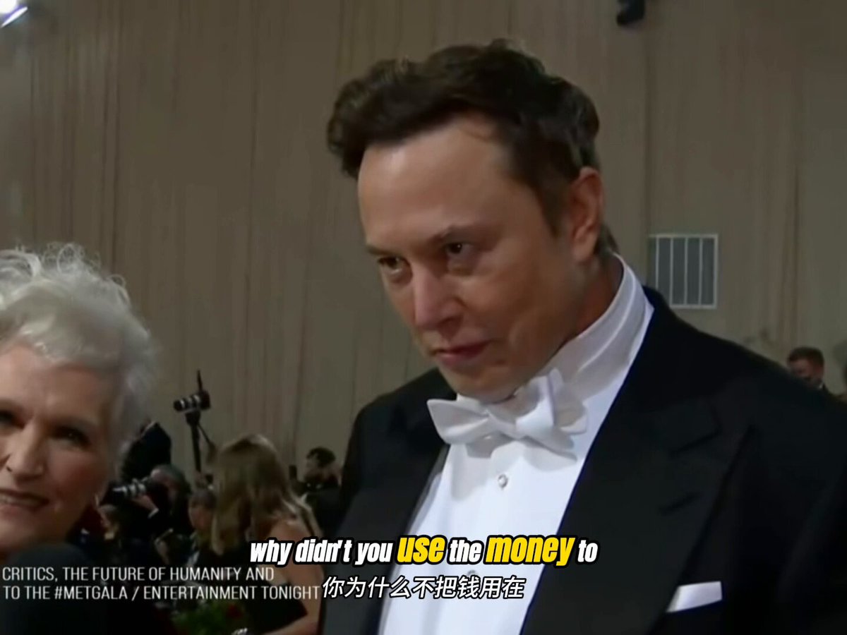 The image shows a man dressed in a tuxedo standing next to an older woman who appears to be wearing glasses. The man has his head tilted back as if he's deep in thought or contemplating something. In the background, there are other people present, but they are not the main focus of the scene.
