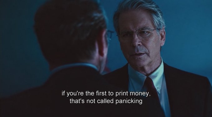 A movie still showing an older man in a suit speaking to another man, with subtitles reading, "if you're the first to print money, that's not called panicking"