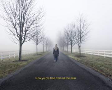 A solitary figure in a dark coat walks down a foggy tree-lined path bordered by white fencing, with the text "Now you're free from all the pain." appearing at the bottom, evoking the melancholic and contemplative mood of the "Keep Me There" photography series auction.