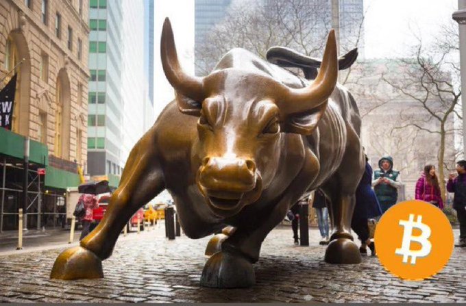 The image features a bronze statue of a bull located on a city sidewalk next to a busy street, with people walking around and buildings visible in the background. The scene also includes an overlay that says "Just In $60,000,000,000 Has Been Addi