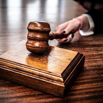 The image features a wooden gavel resting on top of a wooden block or stand. The gavel appears to be made of wood and has a brown color, giving it an antique look. In the background, there are blurred figures that could possibly represent a judge's hand holding the gavel in court. The caption provided suggests that this image is related to a case involving insider trading, as indicated by the post title "LATEST: The US government'S first Insider trading case involving a prediction market heads to trial in December."