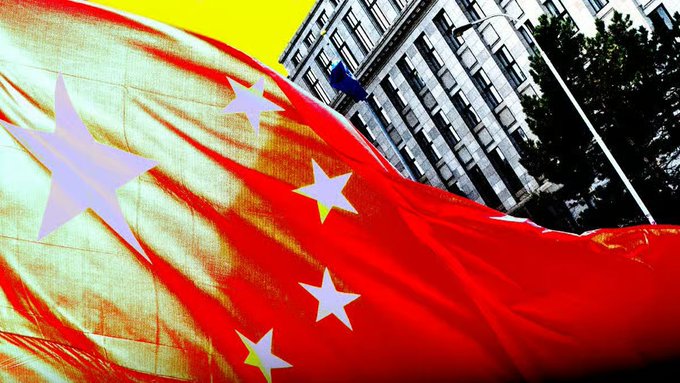 A Chinese flag with its iconic yellow stars waves prominently in the foreground against a stylized backdrop of a government building, symbolizing Saudi Arabia's withdrawal from China's cross-border digital currency initiative in a geopolitical pivot away from Beijing's de-dollarization efforts.