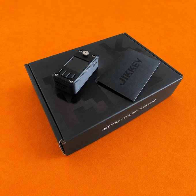 A JIKKEY hardware wallet sits atop its black packaging box on an orange background, with the box labeled "JIKKEY" and "NOT YOUR KEYS, NOT YOUR COINS" alongside a smaller accessory box. This image supports the post announcing JIKKEY's launch in Korea, compatible with both SeedSigner and ShieldSigner, featuring a promotional event offering a USB-C docking battery gift with September purchases.