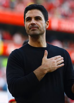 A man in a black sweater stands with his hand over his heart in what appears to be a stadium setting.