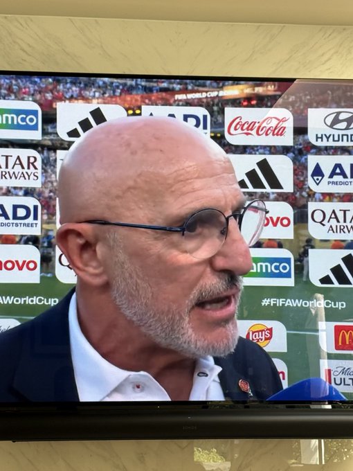 A man with glasses and a beard speaks during a post-match interview at the FIFA World Cup, with sponsor logos including Coca-Cola, Hyundai, Qatar Airways, Adidas, Lay's, and McDonald's visible behind him. Two of the companies shown as World Cup sponsors — Adidas and McDonald's — are listed on the AVAX ticker.