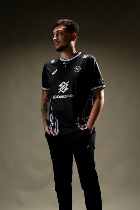 A young man poses confidently in a black soccer jersey featuring "BB CONSÓRCIOS" sponsor text and team crests, reflecting the announcement of joining @fluxogg.