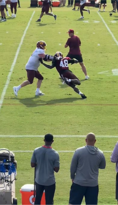 A Washington Commanders practice session shows player #48 stretching his arm out to fend off a defender in a white jersey, demonstrating impressive arm extension and bend as referenced in the caption.