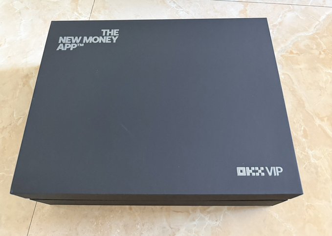 A sleek black premium box labeled 'THE NEW MONEY APP™' with 'OKX VIP' branding sits on a marble surface.