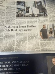 A newspaper page features the headline 'Stablecoin Issuer Tether Gets Banking License,' with a photo of two people and what appears to be a cryptocurrency office above the article.