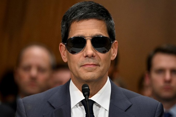 A man in sunglasses and a suit speaks into a microphone at what appears to be a formal hearing or press conference, with other attendees visible in the blurred background. The image likely relates to the post's discussion of US employment data and Federal Reserve policy implications, with the speaker possibly being an economic or financial authority figure commenting on the NFP and unemployment figures.