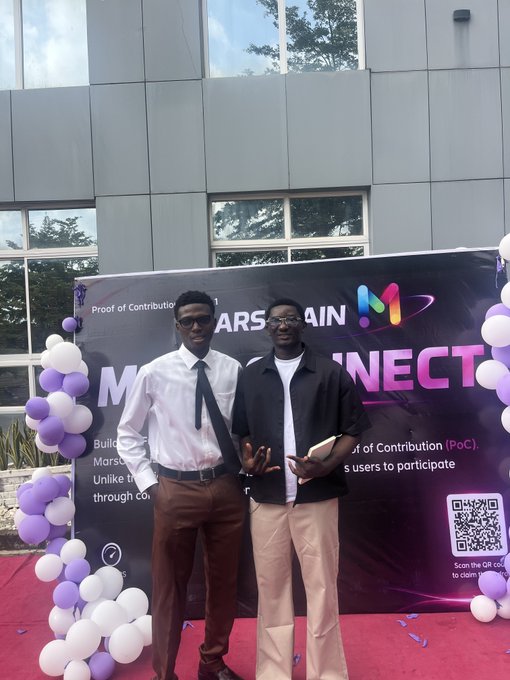 Two young men pose in front of a banner reading 'MARS CHAIN CONNECT' and 'Proof of Contribution,' flanked by purple and white balloon decorations outside a modern building.