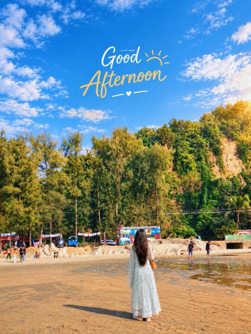 A woman in a long white dress stands on a sandy beach looking out toward the ocean, with the text "Good Afternoon" displayed in the blue sky above trees and rocky cliffs.