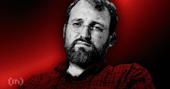 A black-and-white portrait of Cardano founder Charles Hoskinson against a deep red background, with a small "[in]" logo in the lower left, illustrating coverage of his hint about a major Midnight-focused project for the $ADA ecosystem.