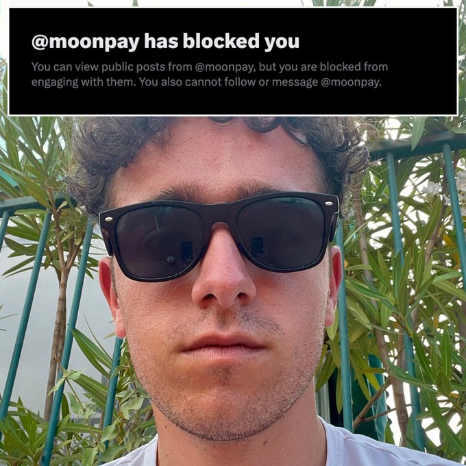 A selfie of a young man wearing sunglasses in front of green foliage, with a Twitter/X notification at the top stating "@moonpay has blocked you."