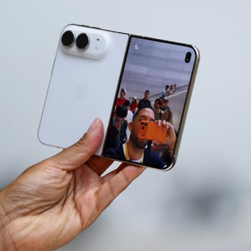 A hand holds a white foldable smartphone (labeled "iPhone Duo" per the post), shown partially open with its cover screen displaying a camera app, illustrating Apple's first foldable iPhone unveiled at around $2,384 or ~0.0305 BTC, contrasted against the BTC valuations of earlier Pro Max models.