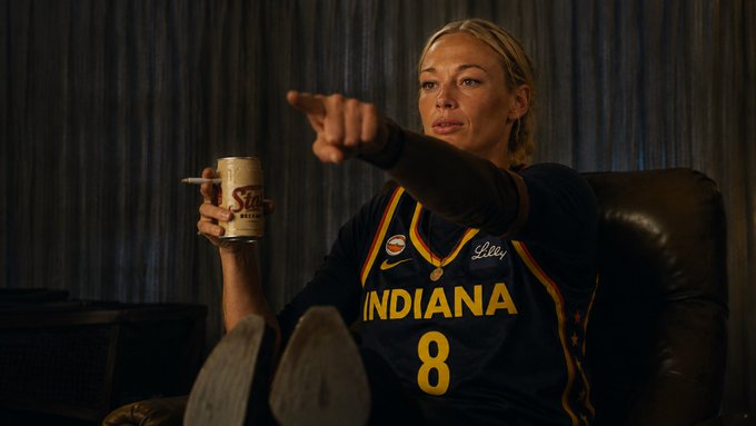 The image shows a woman in an Indiana basketball jersey (#8) holding a beer can and pointing assertively, appearing to be in a casual, lounging setting. Her confident, almost dismissive pointing gesture plays into the meme's joke about her being defensive or gatekeeping her stance on "fungible money," treating the topic with intense focus like she's calling out imposters.
