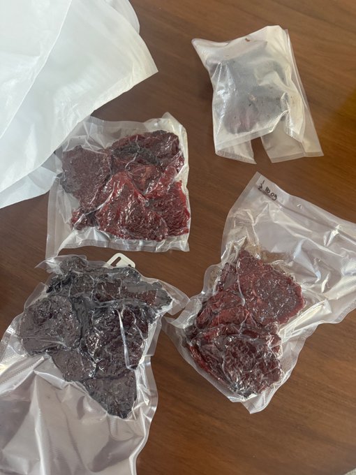 Several clear plastic bags containing dark red dried fruit or jerky are laid out on a wooden surface.
