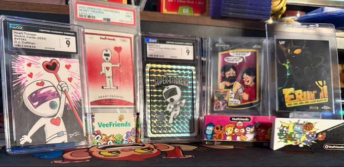 A collection of CGC-graded Veefriends trading cards, including "Hearttronaut," "Heads-Triangles," "Superstitions," and "Erin," with grades of 9 and 9.5, alongside unopened card packs, visually illustrating the saying that a collection is worth a thousand words.