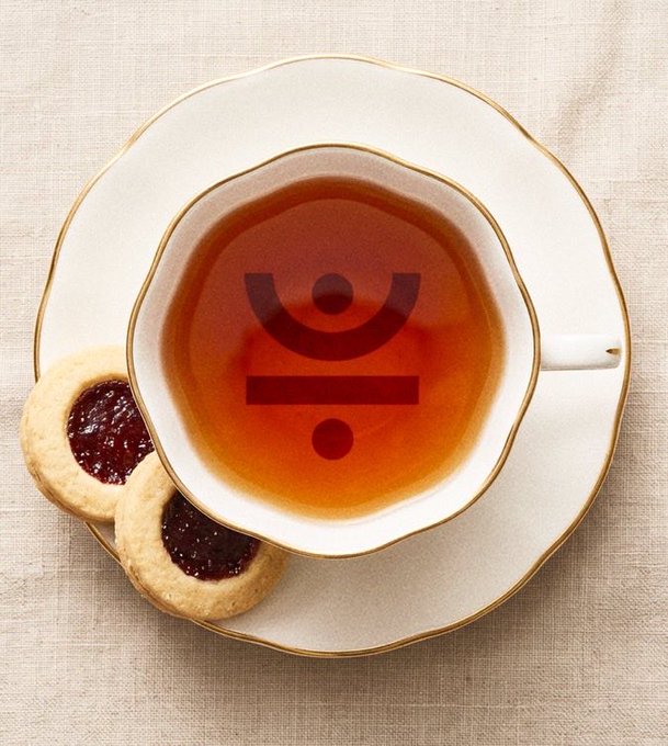 A cup of dark tea sits on a white saucer alongside two jam-filled cookies, with a large red Under Armour logo superimposed in the center of the image.
