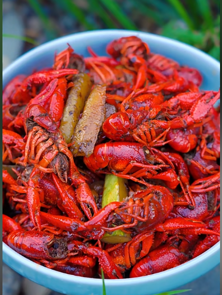 A blue bowl is filled with cooked red crawfish mixed with sausage and corn on the cob.