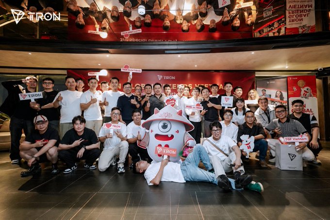 A group of TRON community members and team members pose for a group photo at the "TRON Global Friends Vietnam" 3rd Special Dinner Party in Ho Chi Minh City, with the TRON logo displayed on the backdrop and on handheld signs, alongside a friendly TRON mascot character.

The image directly reflects the caption's description of a warm and meaningful gathering of TRON brothers and sisters from across Vietnam coming together to celebrate their community in Ho Chi Minh City.
