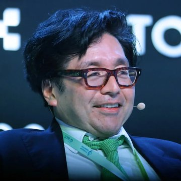 A man with dark hair and red-framed glasses smiles while wearing a headset microphone at what appears to be a conference or panel event. The image appears unrelated to the post, which discusses Kalshi traders forecasting ETH to reach $3.21K.