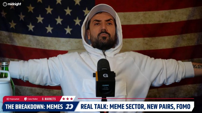 A man in a white hoodie speaking into a 'G' microphone in front of an American flag, with a banner reading 'THE BREAKDOWN: MEMES' and 'REAL TALK: MEME SECTOR, NEW PAIRS, FOMO' alongside Polymarket and Cake Wallet logos.