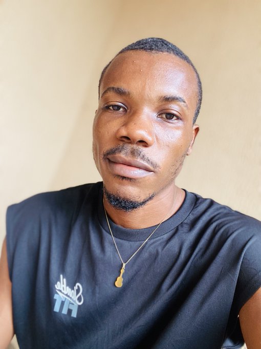 A close-up portrait of a young man with a short goatee wearing a black sleeveless shirt with 'Billabong' branding and a gold pendant necklace.