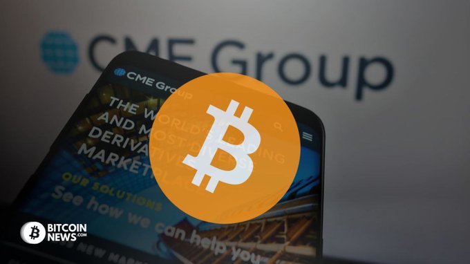The image features a cell phone with an orange Bitcoin icon displayed prominently on its screen. The background of the image reveals a large gray CME Group logo. The text at the bottom of the image provides information about a new trading service that CME is launching, enabling users to trade 24 hours a day with Bitcoin and cryptocurrency options worth approximately $50M.