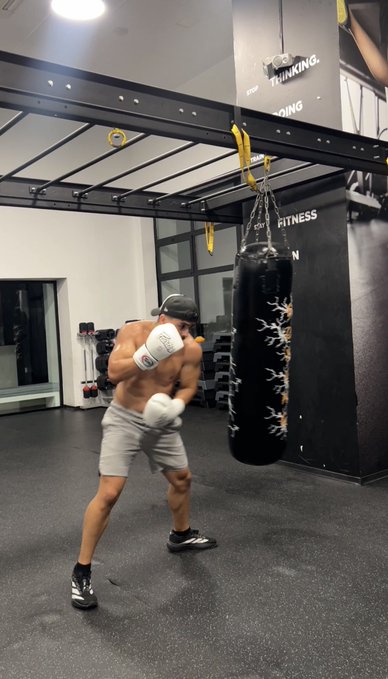 A shirtless, muscular man wearing white boxing gloves throws a punch at a hanging black heavy bag in a modern gym, with the text "THINKING" and "FITNESS" visible on the wall. The image's aggressive training scene visually embodies the post's theme of "preparing for the bull market," symbolizing readiness, discipline, and the fight needed to capitalize on an upcoming uptrend.