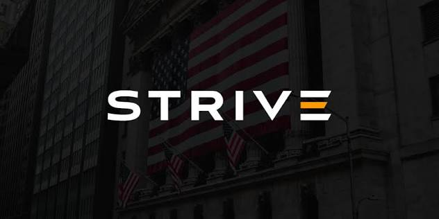 The user wants a concise caption describing the image and its relation to the provided text.

1.  **Analyze the Image:**
    *   **Visuals:** A dark, moody shot of a building facade, likely a financial institution or government building (looks like the NYSE or similar Wall Street building).
    *   **Key Element:** A large American flag is draped over the building.
    *   **Text Overlay:** The word "STRIVE" is prominently displayed in white capital letters. The letter 'E' is stylized with three horizontal bars (orange, white, white - resembling the flag colors or just a logo).
    *   **Context:** The building looks like the New York Stock Exchange (NYSE) due to the columns and the flag arrangement.

2.  **Analyze the Text Prompt:**
    *   The text mentions "Strive continues to purchase an additional 17.76 BTC".
    *   It connects this number