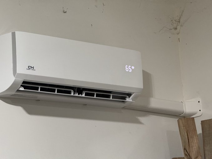 A white wall-mounted Cooper & Hunter (CH) ductless mini-split air conditioner is installed near the ceiling, displaying a temperature reading of 65° on its digital panel, with the refrigerant line set running along the wall to the right.