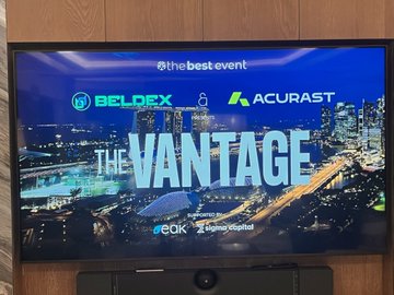 A television screen displays an event titled 'THE VANTAGE' hosted by the best event, with sponsors BELDEX and ACURAST visible, showing a cityscape background and 'Sponsored by QOIX Gaming eGadget' text.