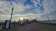 urns on a wooden pier, with a large building and trees in the background, under a blue sky with white clouds.