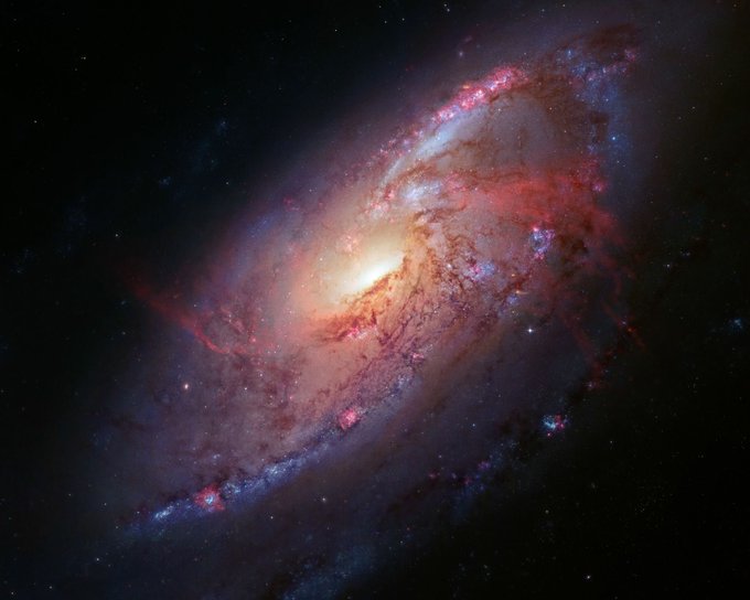 A stunning astronomical image of a spiral galaxy featuring a bright yellow core surrounded by swirling arms of pink and blue cosmic dust and stars.