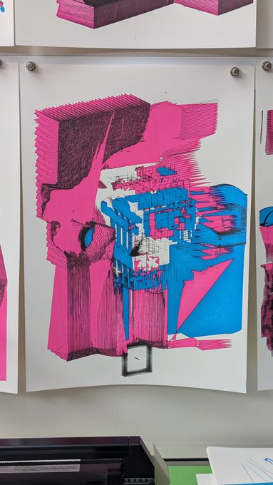 An abstract artwork featuring bold pink and blue geometric shapes hanging on a white wall, with a printer and papers visible at the bottom of the frame.