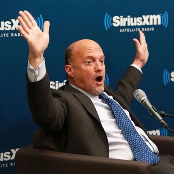 A bald man in a suit and blue tie gestures animatedly while speaking at a SiriusXM Satellite Radio interview with a microphone visible.