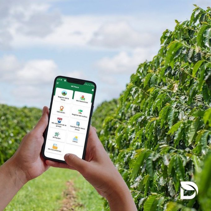 Hands holding a smartphone displaying the 'Mi Finca' agricultural app with Spanish menu options like 'Registro de la Finca' and 'Ubicación', set against a backdrop of green crops.