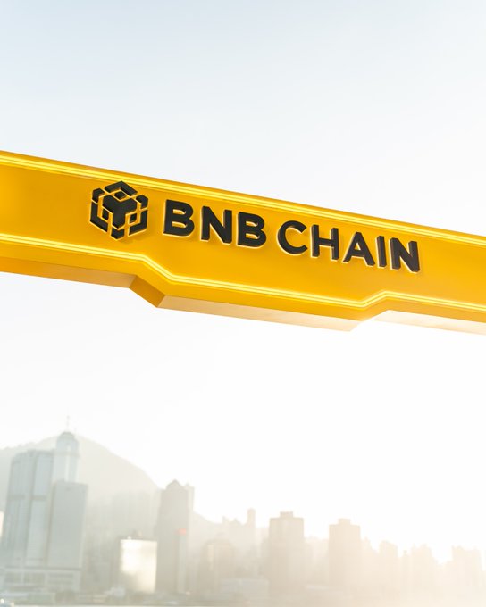 A bright yellow "BNB CHAIN" banner floats above a hazy city skyline, promoting the upcoming 24-hour countdown to #BNBTokyo, an event celebrating the vibrancy of the BNB ecosystem. The bold branding ties directly to the post's invite to join the lively evening gathering.