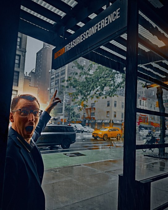 A dramatic photo of a man with glasses shouting excitedly and pointing upward at a 'BITCOIN TREASURIES CONFERENCE' sign on a rainy New York City street, with yellow taxis visible in the background.