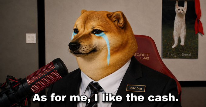 A Shiba Inu dog wearing a suit and tie cries blue tears while sitting in front of a microphone, with a caption reading "As for me, I like the cash." and a name tag labeled "Debt Dog." In the background, a poster of a cat reads "Hang in there!" — contrasting the cash-stressed, tearful dog with the hopeful, motivating cat, directly tying into the post's message that the dog lacks the cash the cat symbolizes.