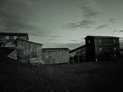 A moody, dark-toned landscape showing old wooden buildings under an overcast sky.