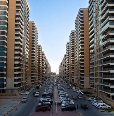 A row of tall residential towers lines a street filled with parked cars under a clear sky, with no visible text or signage. The image appears unrelated to the accompanying post, which discusses arrests and financial corruption in Iraq's Building 22, as no such building, text, or identifying features are present.
