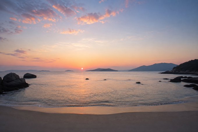 A serene sunrise over a calm beach with scattered rocks and distant mountains, the soft pastel sky reflecting on gentle waves. The peaceful dawn scene mirrors the post's hopeful message of starting Friday fresh and focusing on building, encouraging resilience despite the recent downturn in the crypto market.