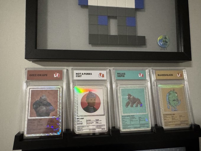 A framed pixel art piece displayed above four graded/traded NFT cards in protective slabs, including 'GEEZ ON APE', 'NOT A PUNKS CULT', 'RILLAZ DEPOT', and 'BLAZER-GLAZE'.