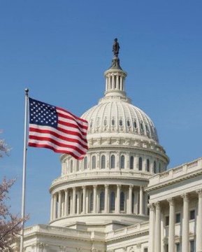 The U.S. Capitol building dome is shown against a clear blue sky with an American flag waving in the foreground.